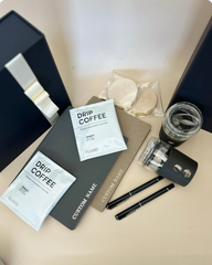 Drip coffee packets, IoCo Eco-Glass Traveller, and a notebook on a light surface, With black giftbox and Dior bow.